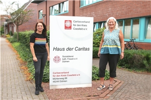 079-2020_Adoptionsvermittlung_SkF_Dülmen Zwei Frauen stehen neben einem Plakat des SkFs Dülmen.