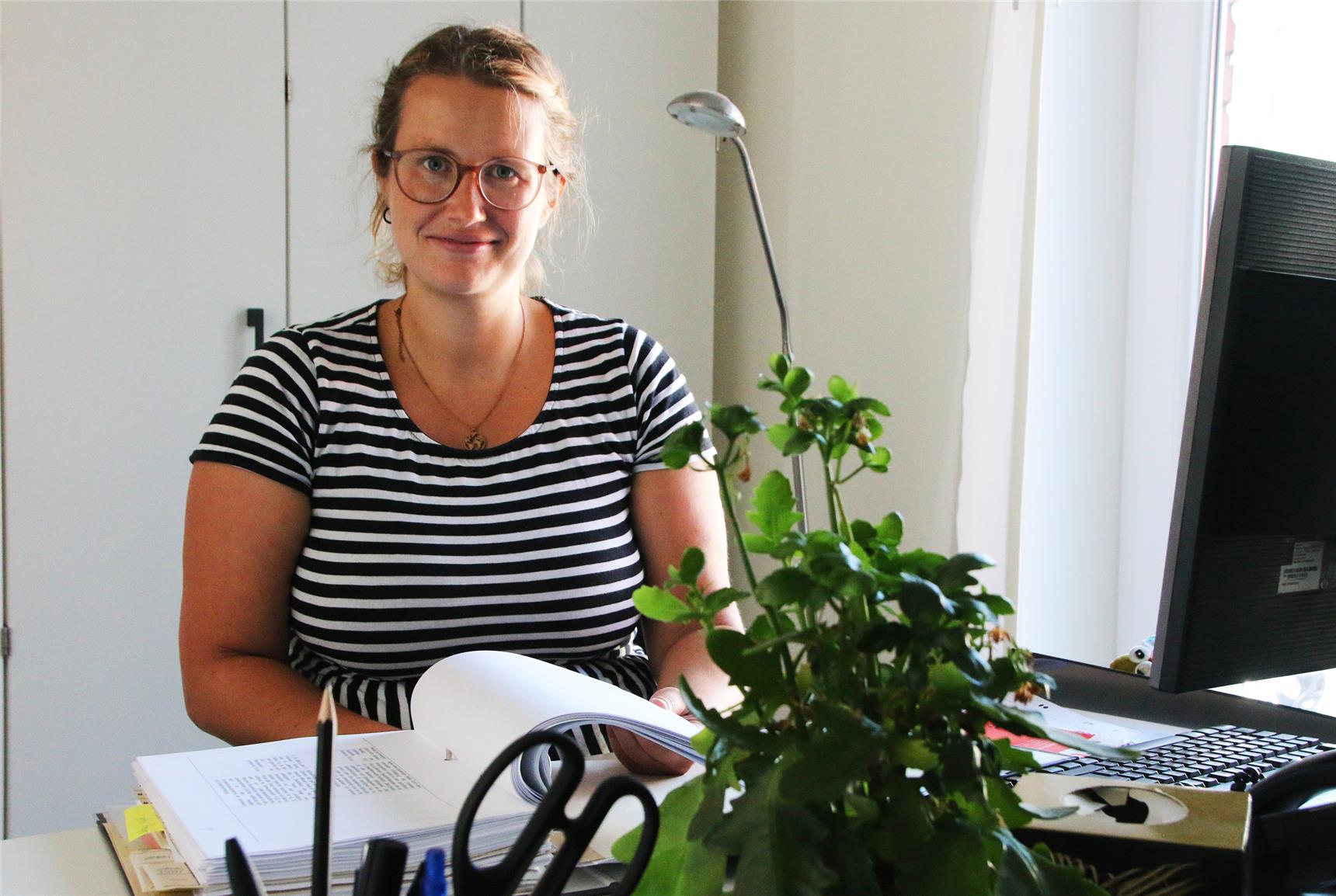 Eine Frau sitzt am Schreibtisch und blättert in einem Ordner.