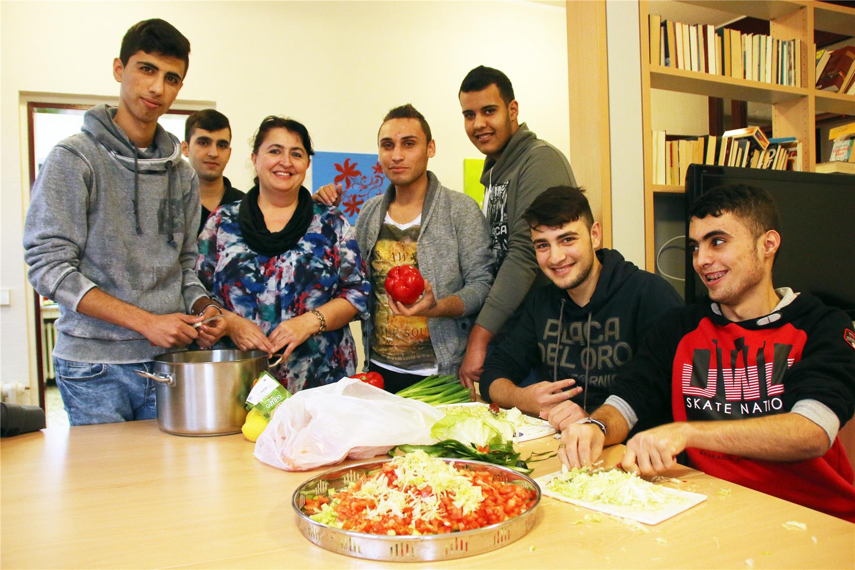 Sechs Jungen und eine Frau schneiden an einem Tisch Gemüse.