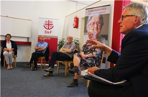 086-2020_Projekt Altersarmut Fünf Personen sitzen in einem Stuhlkreis. Im Hintergrund stehen Plakatwände vom SkF.