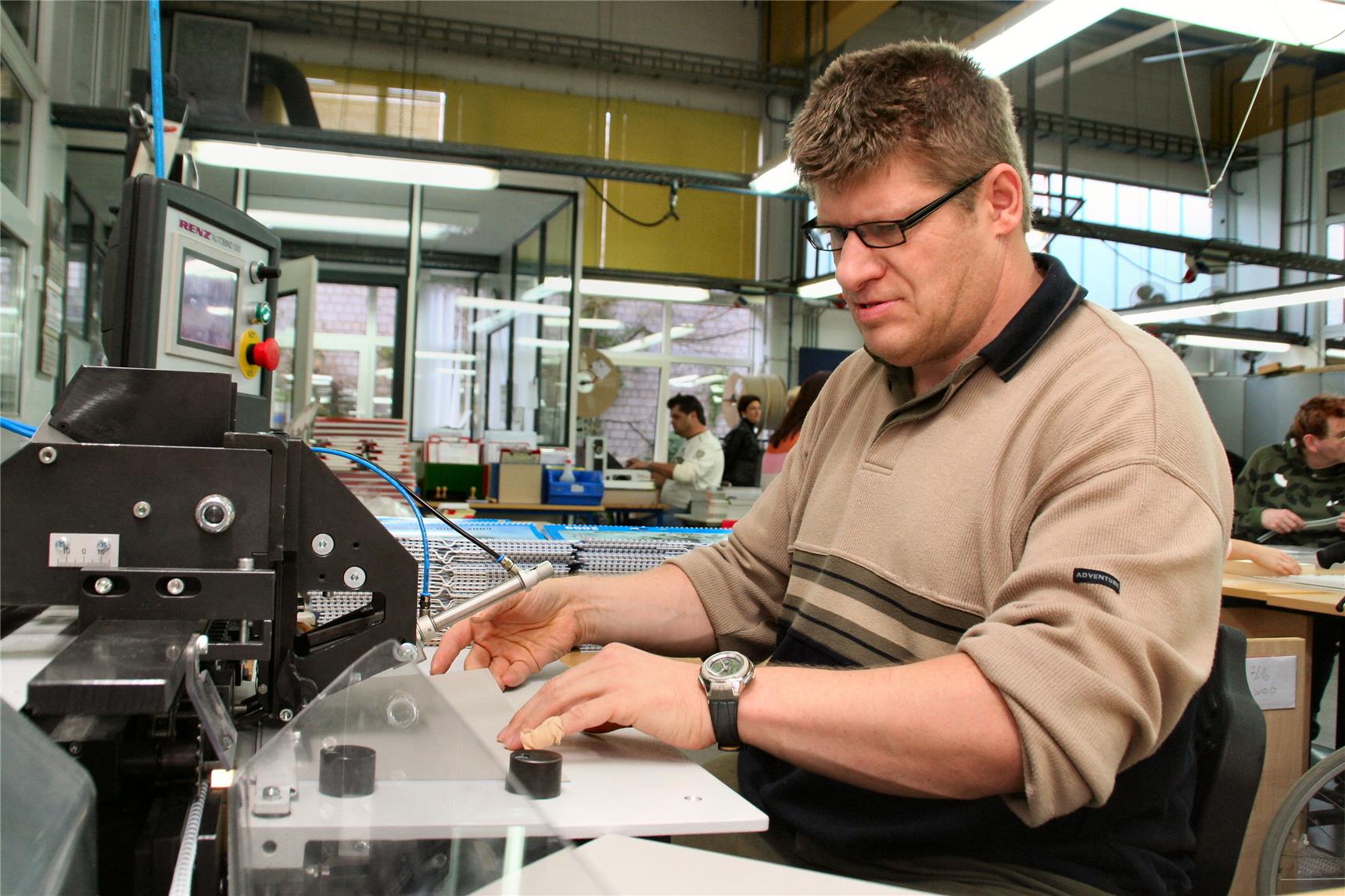 Das Foto zeigt einen Mann in einer Behindertenwerkstatt an einer Maschine sitzend.