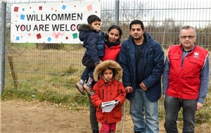 008-2022 Familiennachzug Das Foto zeigt eine Flüchtlingsfamilie vor einem Willkommensschild.