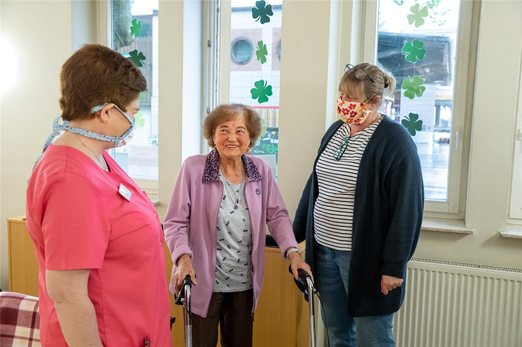 Das Foto zeigt eine Altenheim-Bewohnerin im Gespräch mit zwei Betreuuerinnen.