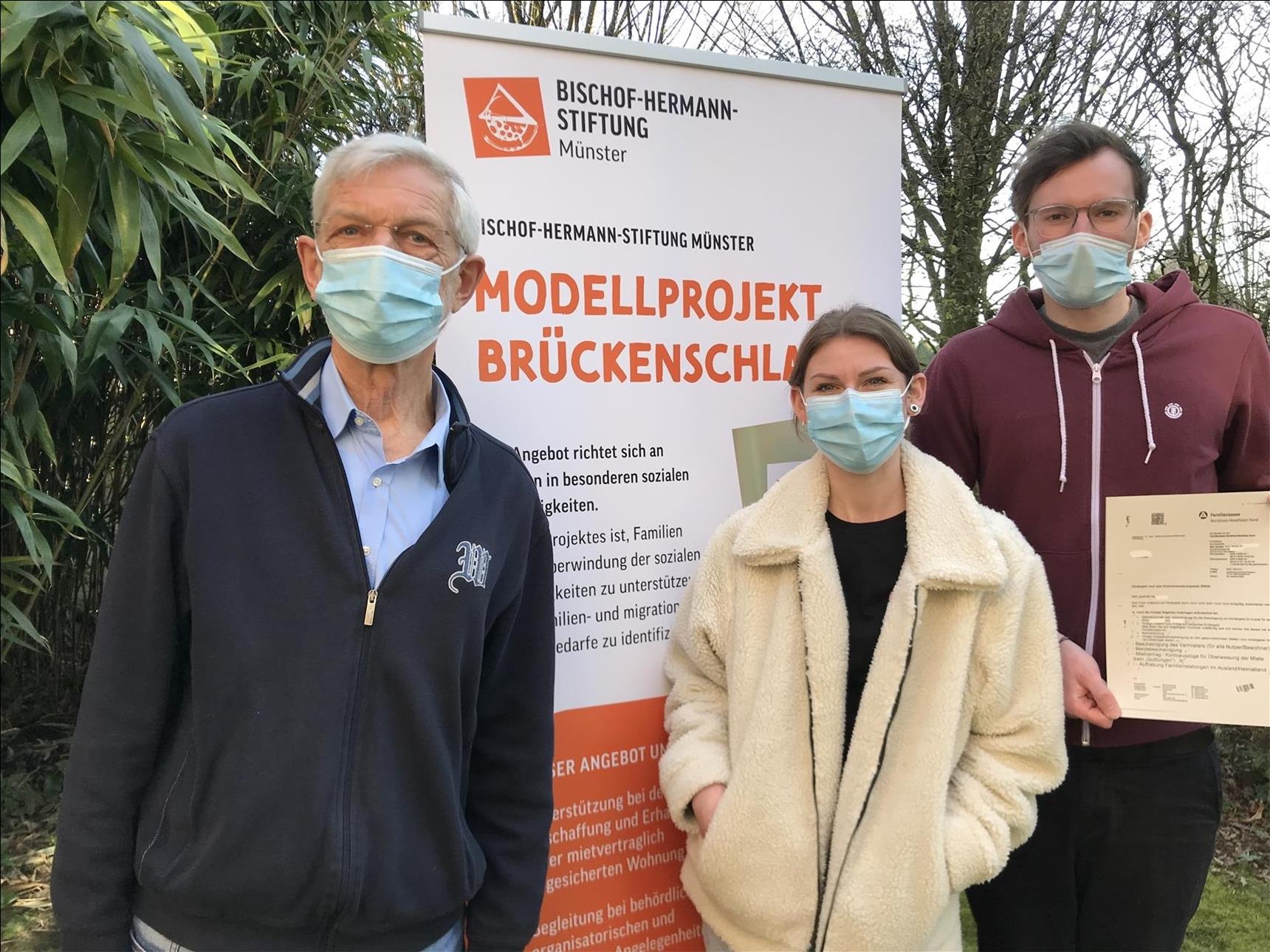 Drei Mitarbeiter stehen vor dem Rollup des Projekts Brückenschlag.