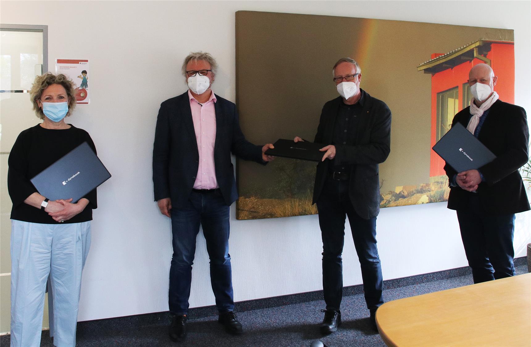 Das Foto zeigt vier Menschen mit Masken auf, die Laptops in den Händen halten.
