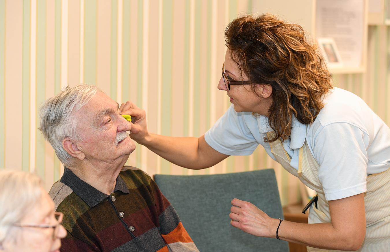 Auf dem Bild sieht man eine Dame, die einen älteren Herren pflegt.