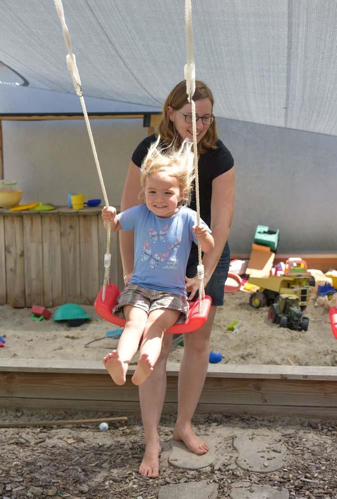 Das Foto zeigt eine Mutter, die ihrem Kind auf einer Schaukel Anschwung gibt.