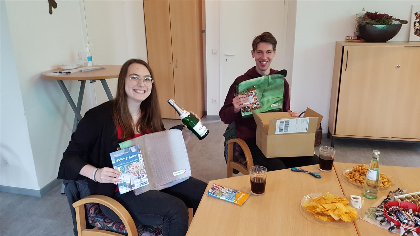 Das Foto zeigt zwei junge Erwachsene, die sich freuen und dabei eine Sektflasche in die Höhe halten.