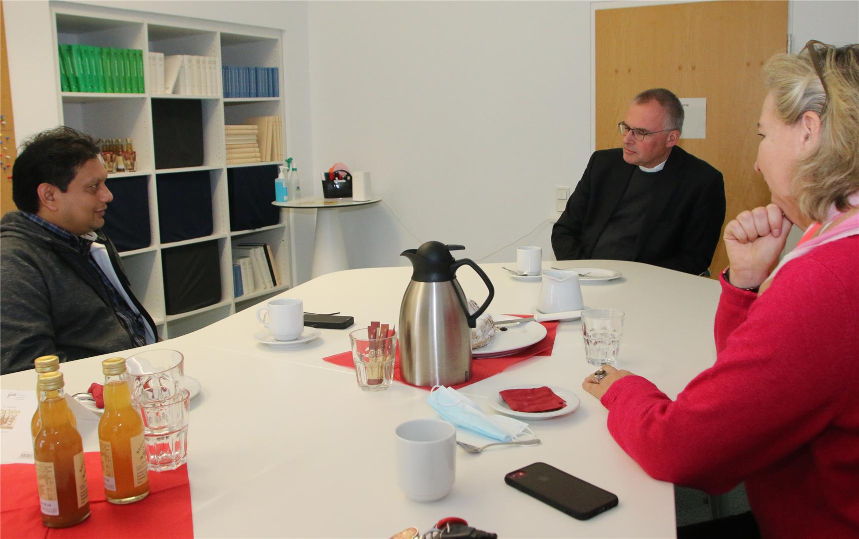 Das Foto zeigt drei um einen Tisch versammelte Menschen im Gespräch.