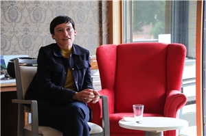 61-2021 Trainee-Gespräch Frau Josefine Paul sitzt auf einem Stuhl, vor einem kleinen Tisch. Neben ihr steht ein roter Sessel.