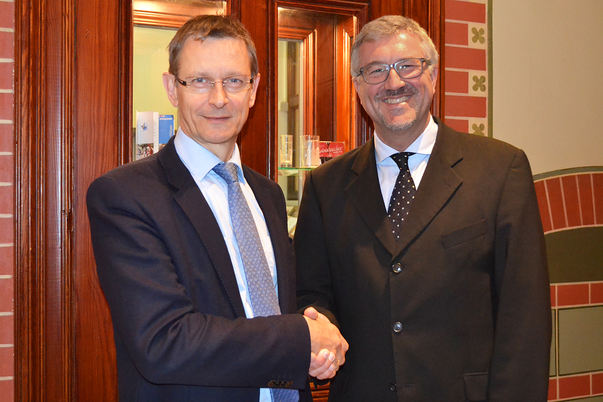 Dr. Frank Johannes Hensel und Christian Heine-Göttelmann stehen nebeneinander, geben sich die Hand und lächeln in die Kamera