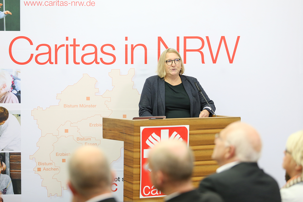 Essens Diözesan-Caritasdirektorin Sabine Depew steht beim Ruhrgebietstag vor einem Rednerpult und hält ihre Begrüßungsrede. Neben ihr ist ein Faltdisplay der Caritas in NRW zu sehen.