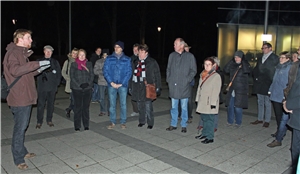 Armutsspaziergang Gruppe steht auf dunklem Platz. Eine Person spricht.