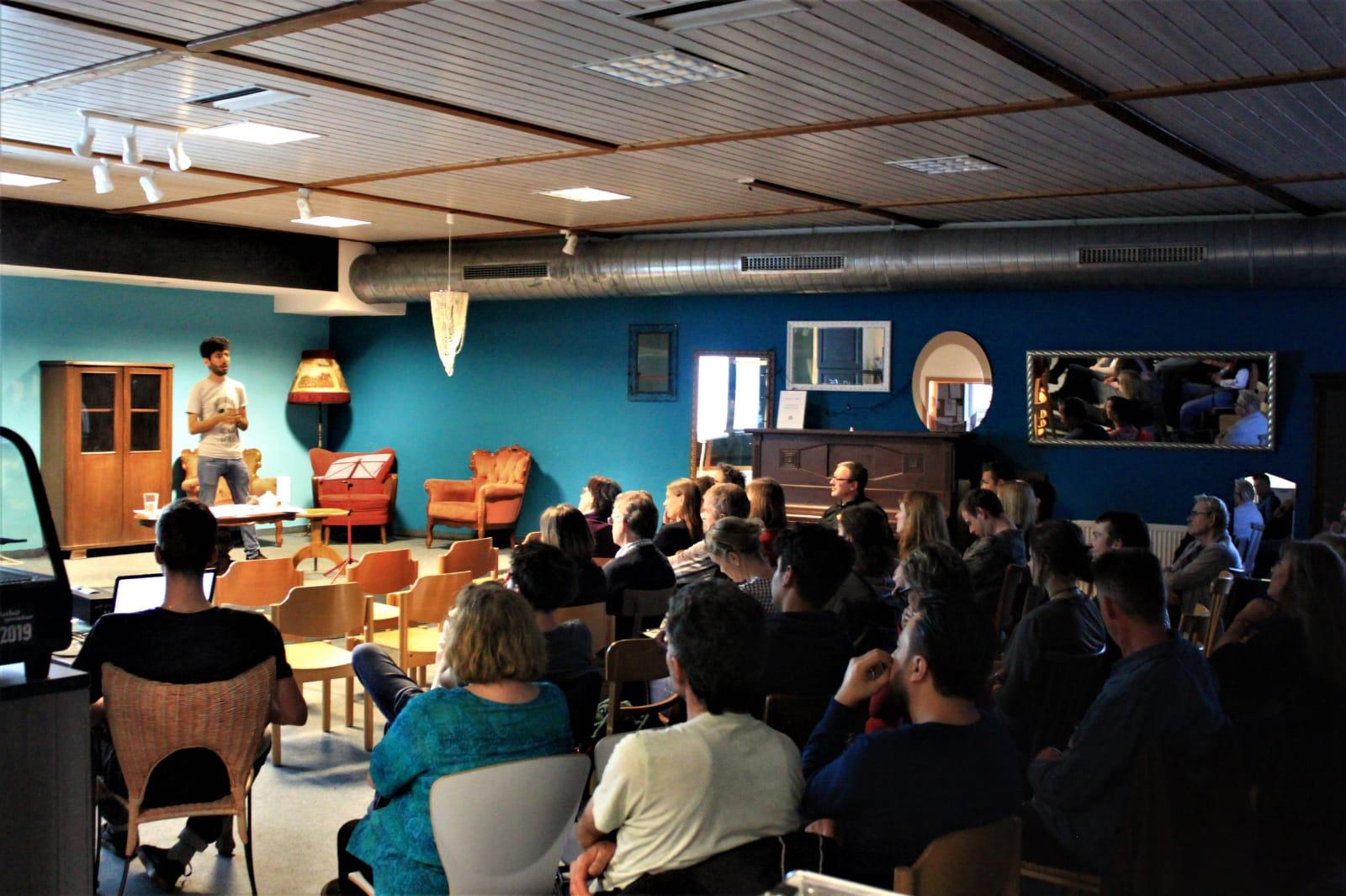 Ein junger Mann steht vor einem gefüllten Klassenraum.