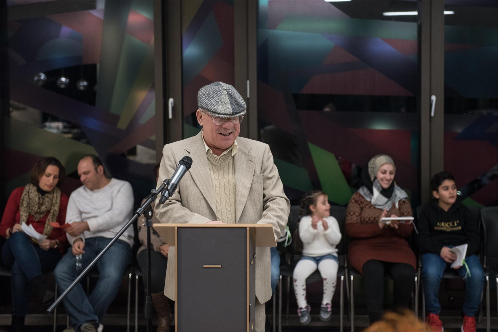 Ein älterer Mann steht an einem Pult und liest etwas vor.