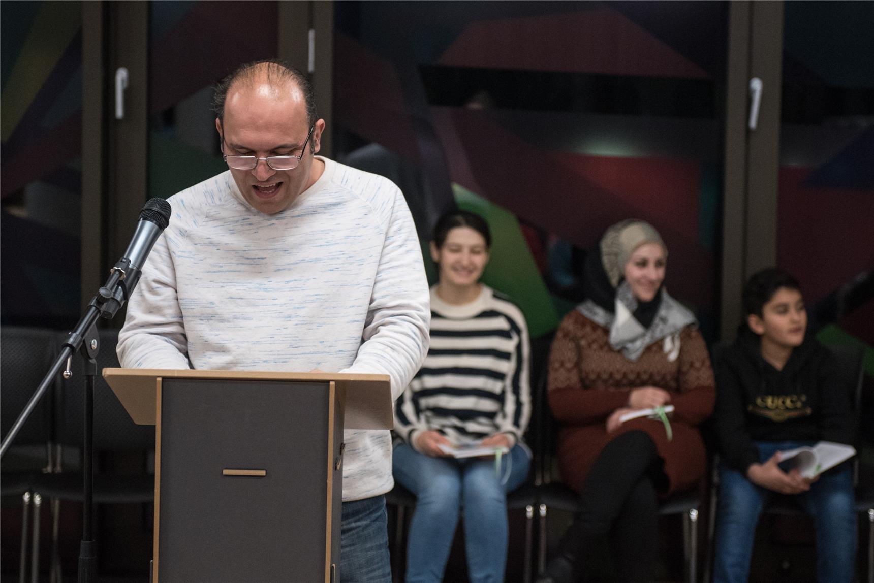 Ein Mann mit Brille steht an einem Pult und liest einen Text vor.