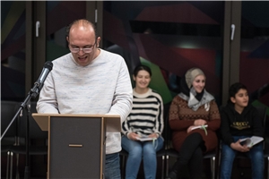 Fürth_Hossein_Ein_Engel Ein Mann mit Brille steht an einem Pult und liest einen Text vor.