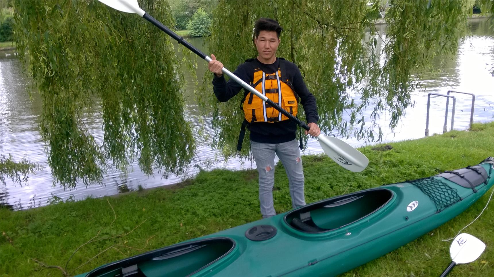 Ein Junge mit einem Paddel in der Hand steht vor einem Kajak