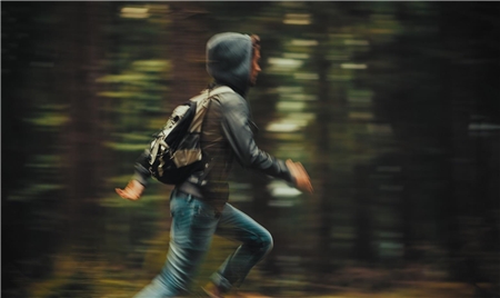 Symbolbild_Flucht allein Ein Jugendlicher mit Kapuzenpullover, Rucksack und Jeans rennt durch einen Wald.