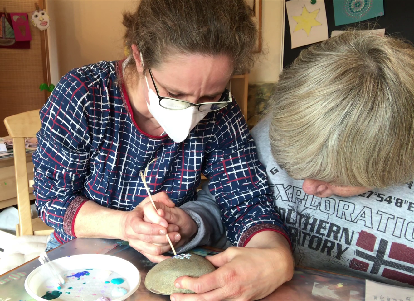 Heilerziehungspflegerin unterstützt Bewohnerin beim bemalen eines Steins.