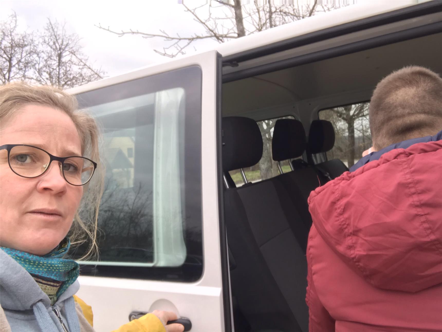 Frau mit Brille unterstützt jungen Mann beim einsteigen in einen Bus. 