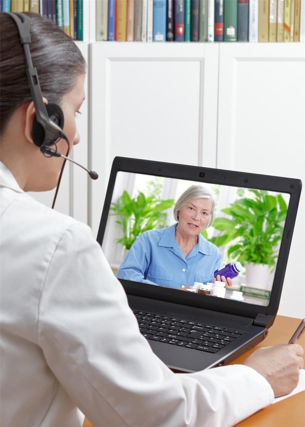 Eine ältere Dame ist über Bildschirm-Telefon am Rechner mit einer jüngeren Beraterin verbunden.