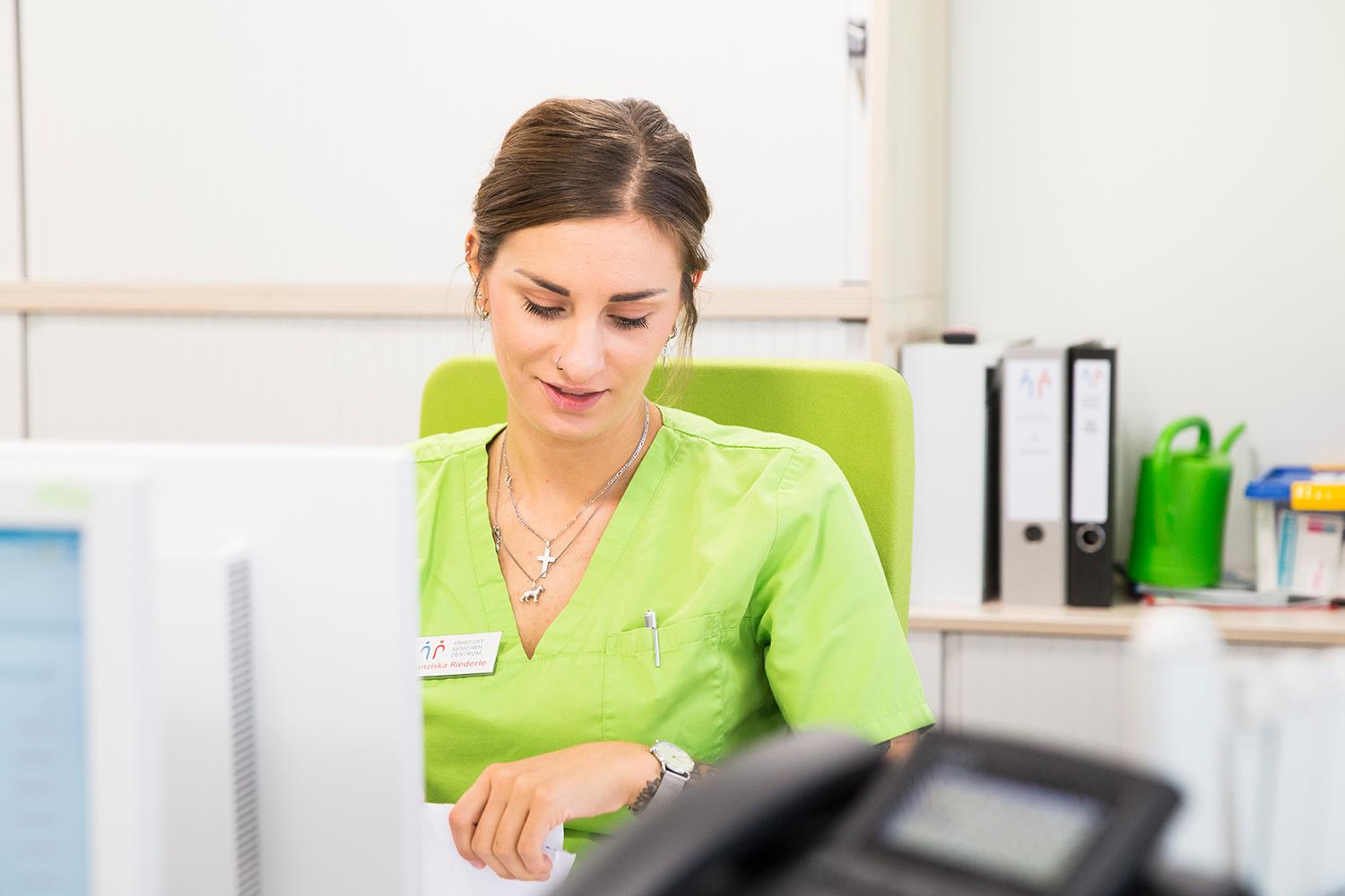 Eine Pflegekraft sitzt am Schreibtisch vor dem Computer