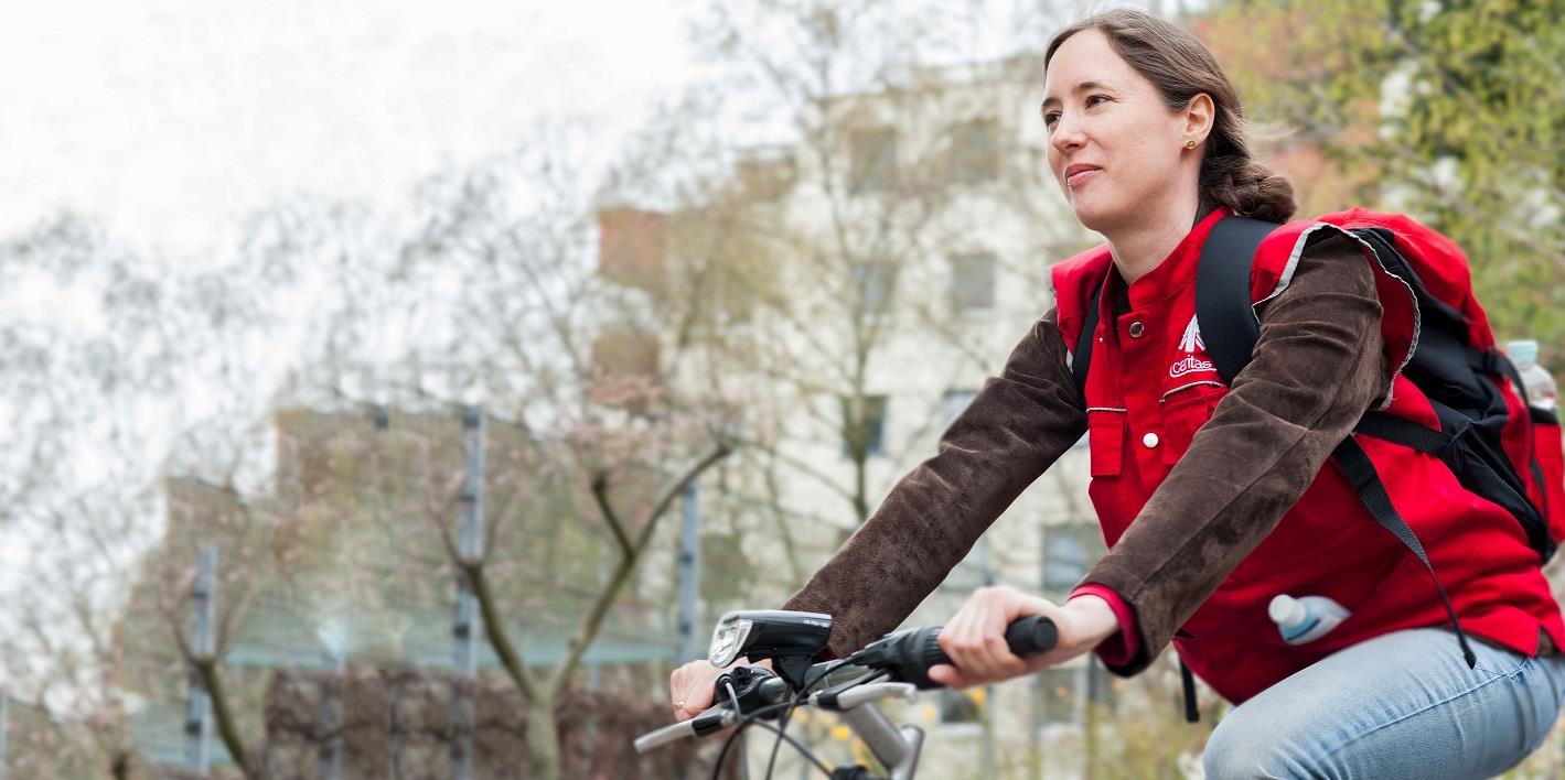 Frau mit Caritas-Weste auf einem Fahrrad
