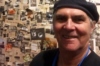 Älterer Mann mit schwarzer Mütze vor einer Fotowand.