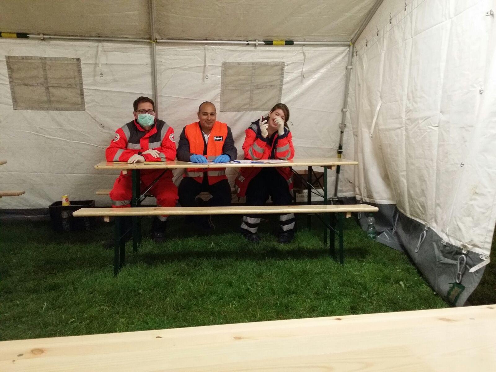 Zwei Mitarbeiter des Deutschen Roten Kreuzes sitzen gemeinsam mit einem Herrn an einer Bierzeltgarnitur in einem Rettungszelt.