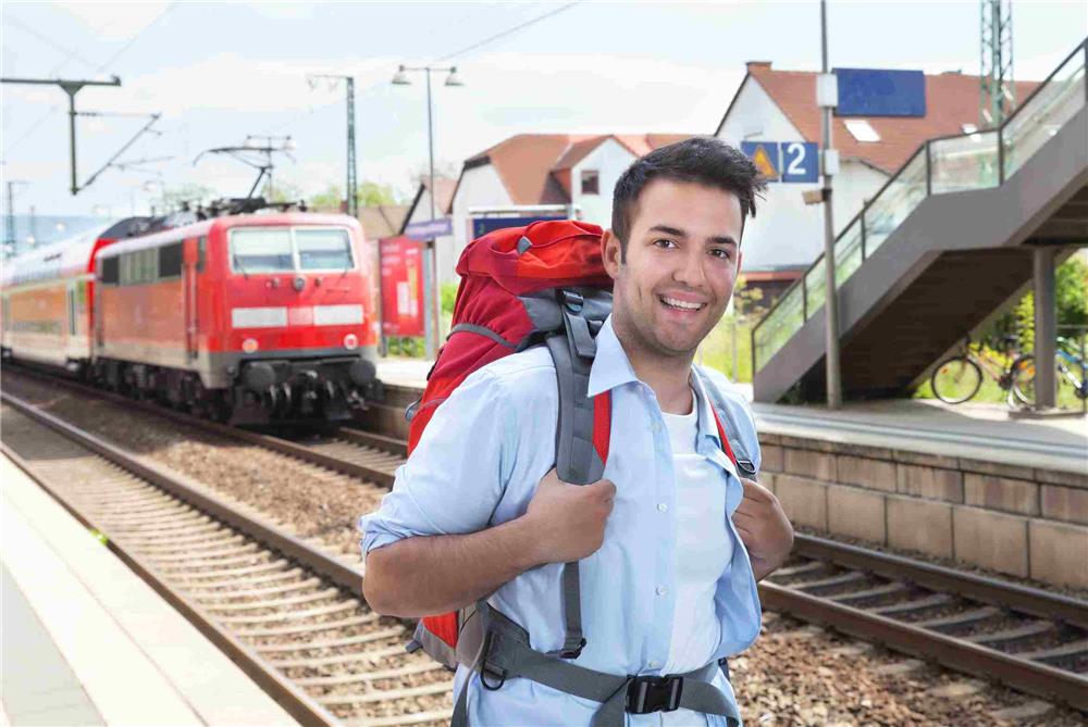 Lächelnder Mann mit Wanderrucksack am Bahnsteig