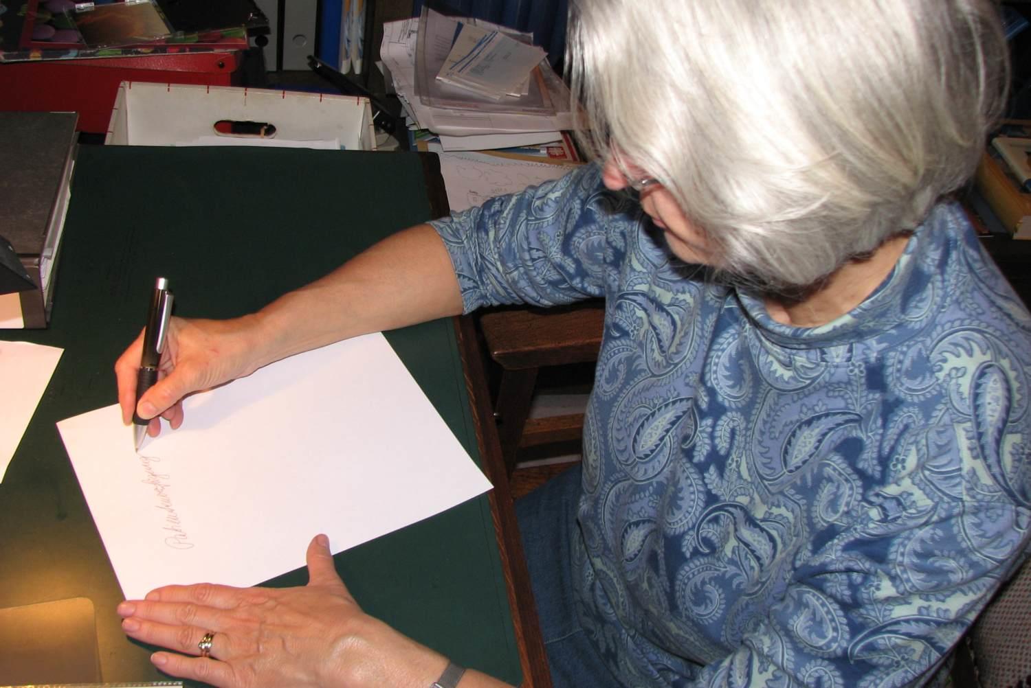 Eine rund sechzigjährige Dame beginnt ein Blatt Papier auszufüllen.