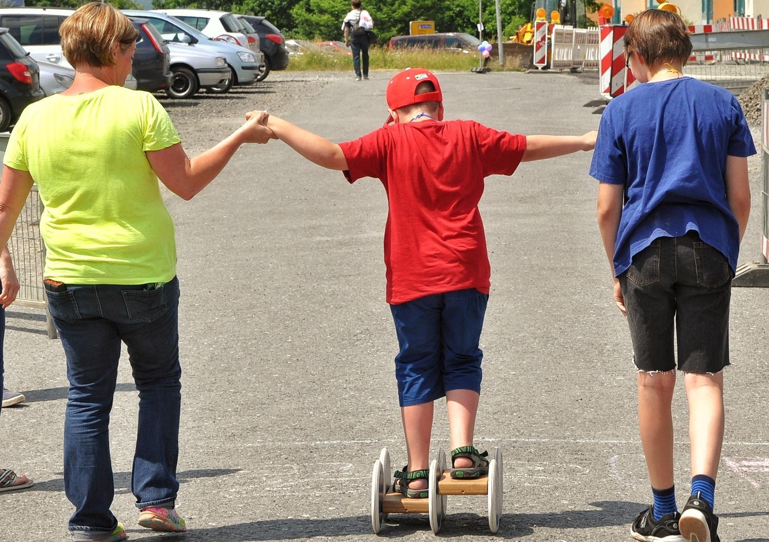 Eine Trainerin stützt ein Kind auf einem Roller.