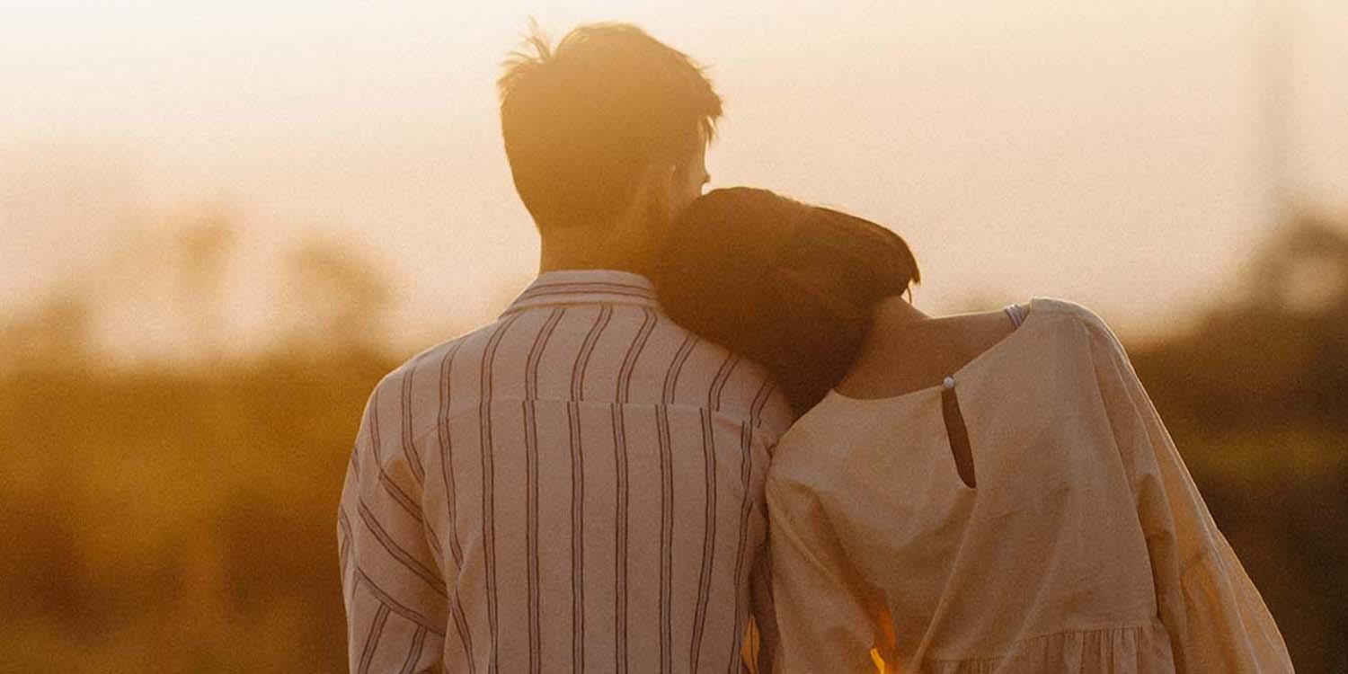 Glückliche Beziehung Symbolbild 1500x750 Eine junge Frau lehnt sich an die Schulter eines jungen Mannes.