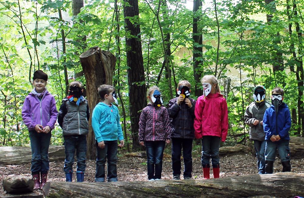 Kinder mit selbstgebastelten Masken im Wald.