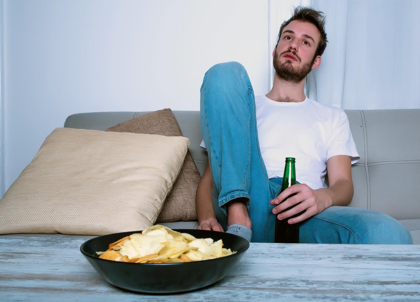 Junger Mann auf Sofa mit Bier in der Hand