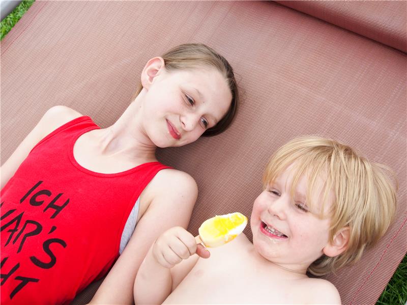 Ein kleiner Junge schleckt fröhlich sein Eis, während die große Schwester ihm dabei zuschaut.