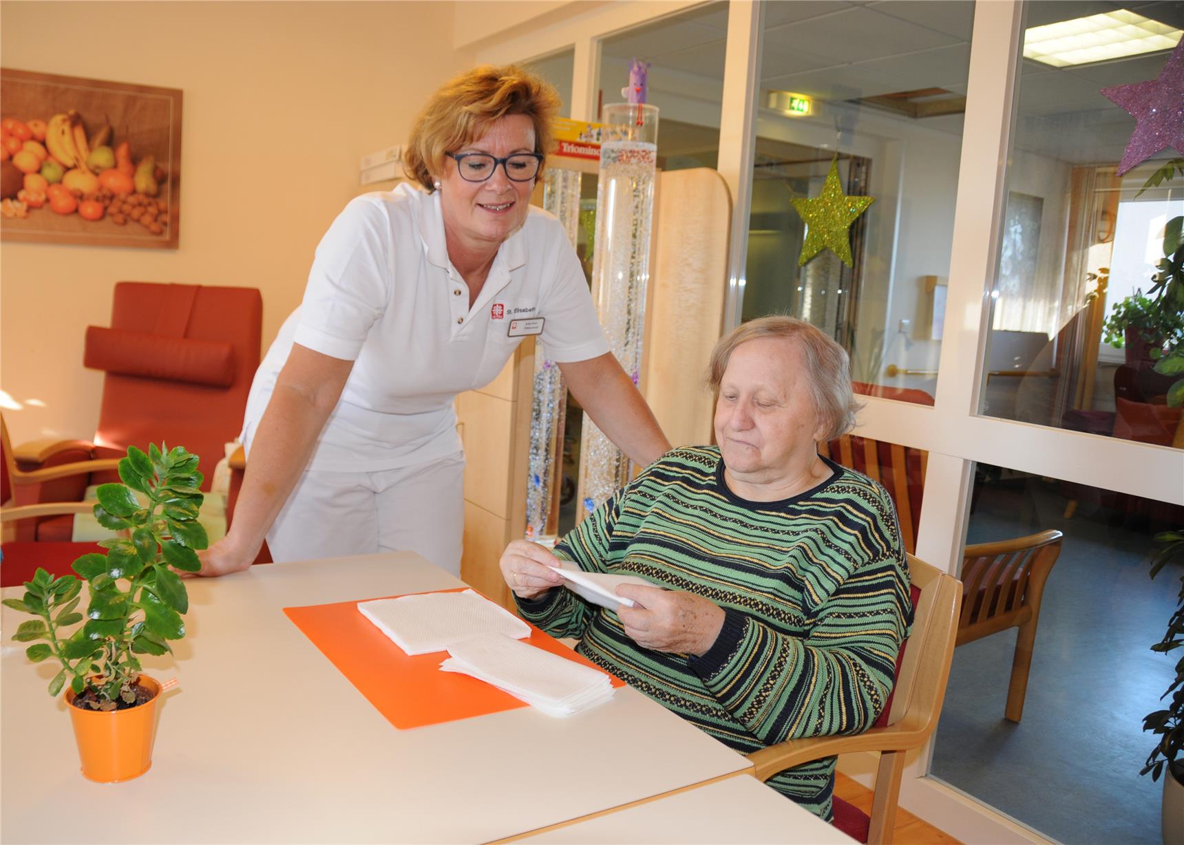 Alte Frau faltet in Anwesenheit von Präsenzkraft Serviette