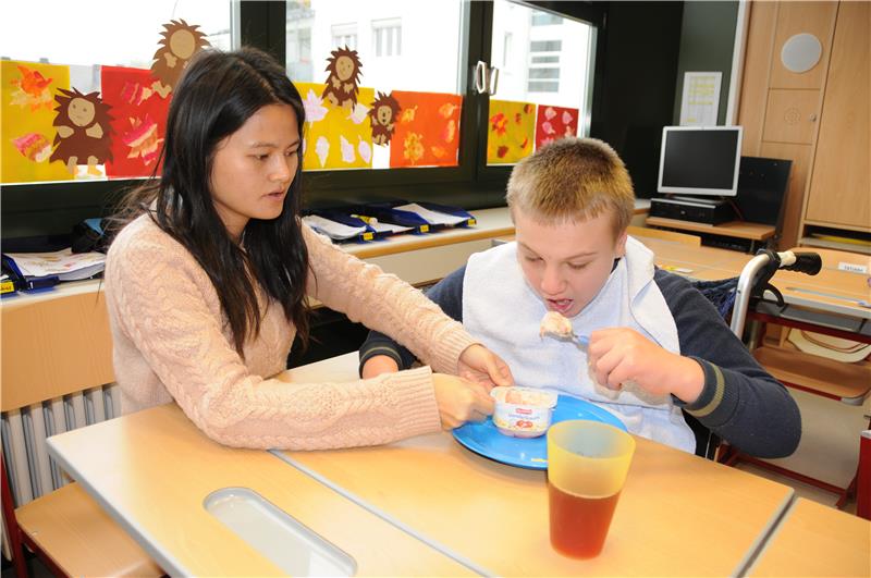 Chinesische Bundesfreiwilligendienstleistende hilft Jungen mit Behinderung beim Essen