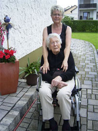 junge Frau schiebt alte Frau im Rollstuhl