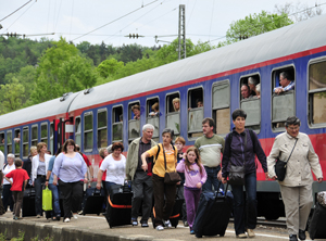 Leute mit Gepack auf Bahnsteig vor Zug mit Leuten