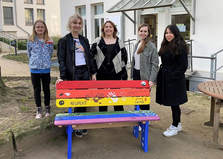 Ein Team junger Menschen steht hinter einer bunt gestalteten Bank