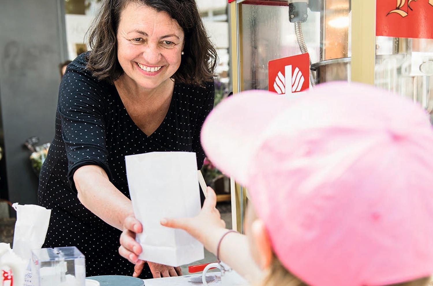 Caritas-Mitarbeiterin Gertrud Klopsch überreicht einem Kind eine frisch befüllte Popcorn-Tüte.