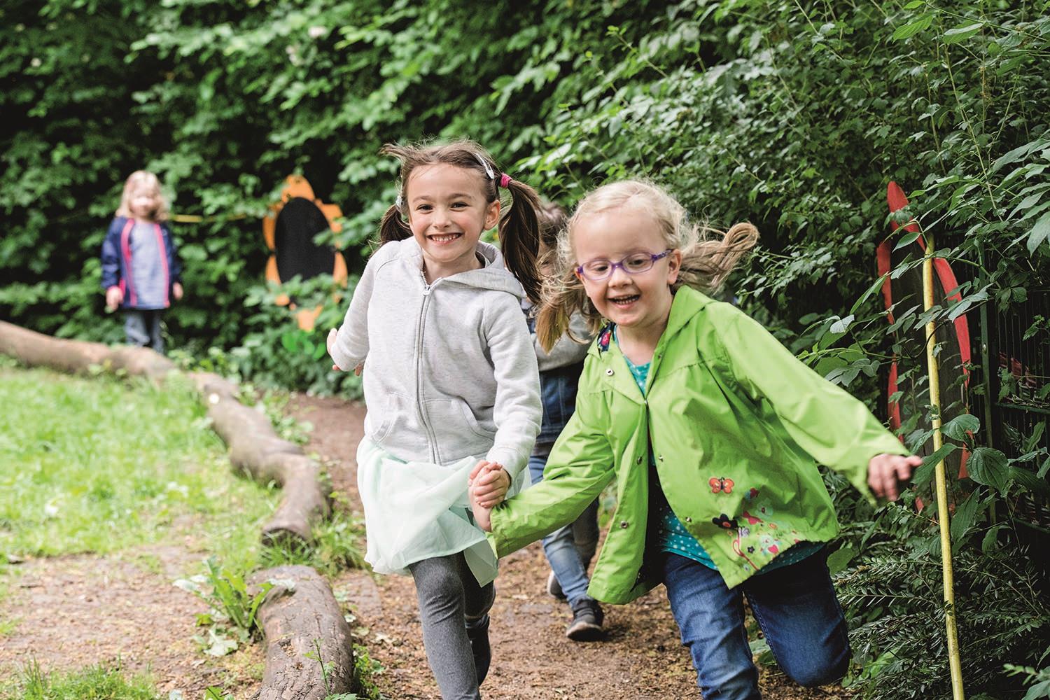 Zwei Mädchen rennen durch den Gartenbereich ihres Kindergartens.