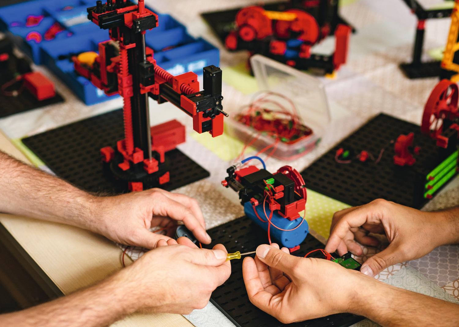 zwei Paar Männerhände beim Bauen mit einem Bausatz von Fischer-Technik