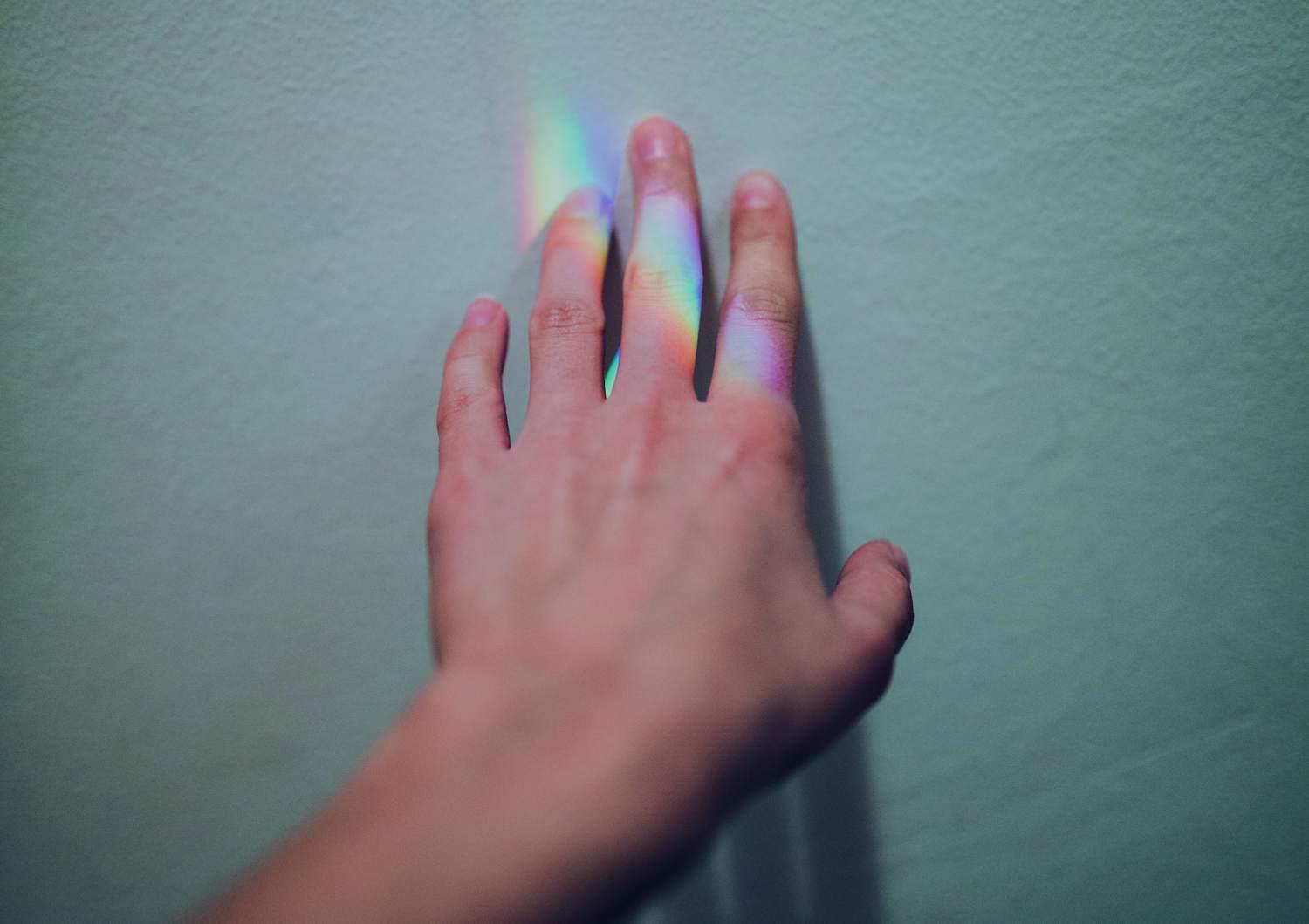 Eine Kinderhand vor einer Wand wird von den Regenbogenfarben eines Prismas beleuchtet.