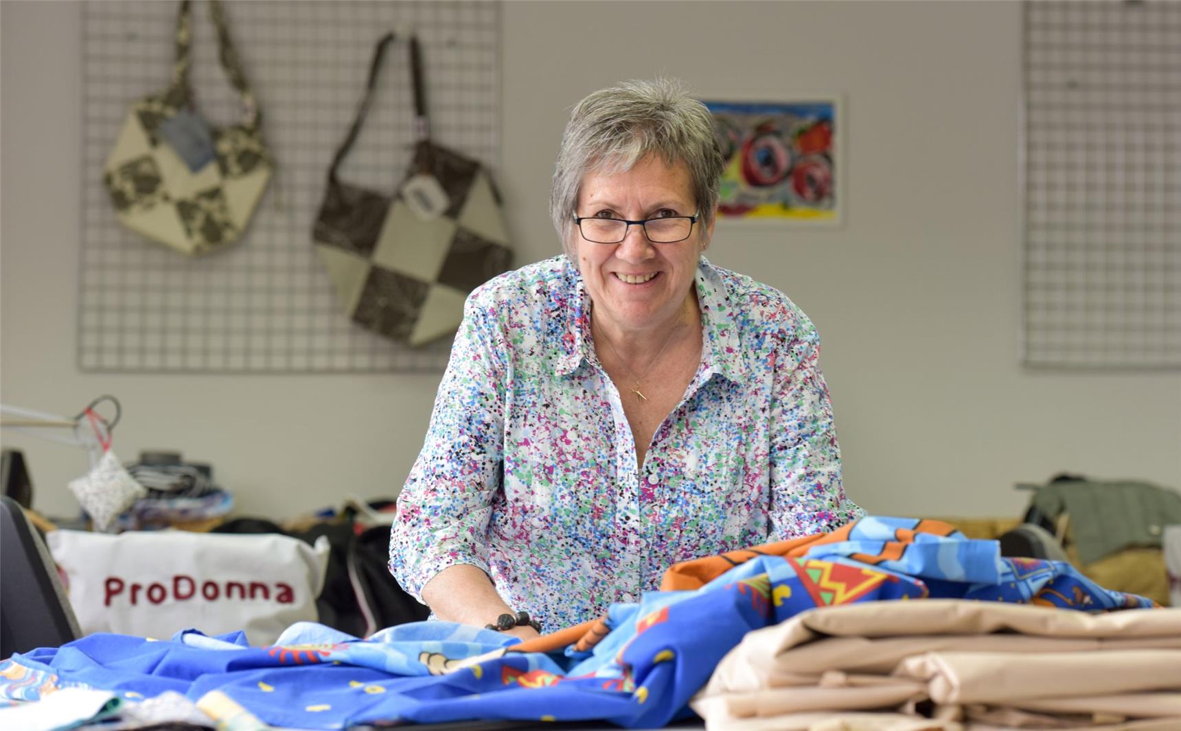 Eine Mitarbeiterin von ProDonna blickt an ihrem Arbeitsplatz vom Stoffe-Zuschneiden auf.