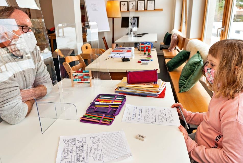 Eine Schülerin mit einem Lehrer, durch eine Plexiglasscheibe von ihr getrennt, bei den Mathehausaufgaben.