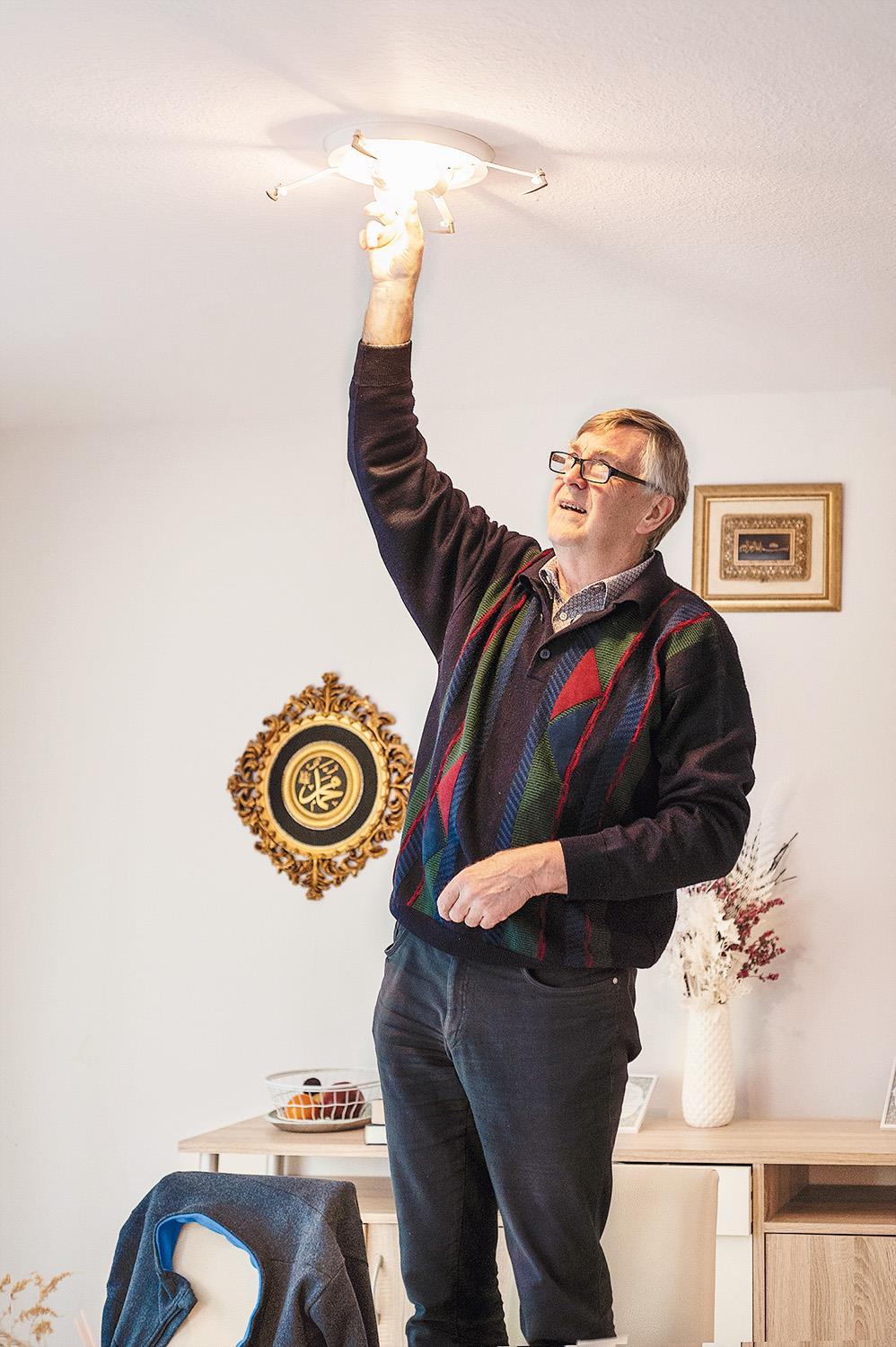 Stromsparhelfer Wilken steht auf einer Leiter und prüft die Deckenleuchten