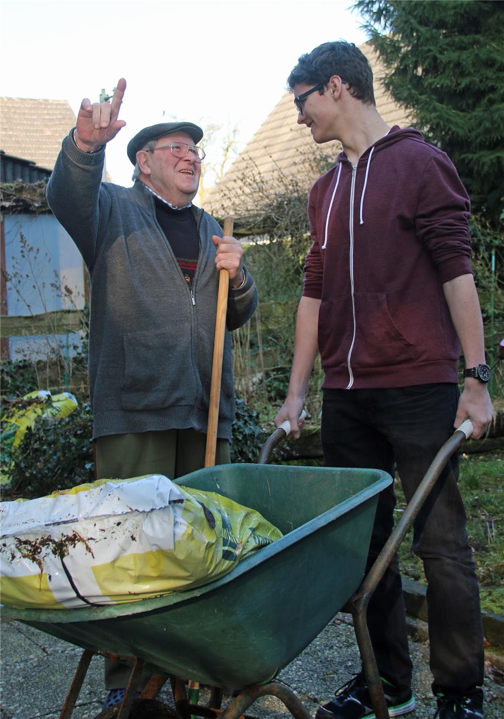 Ein älterer Herr mit einem jüngeren Mann, der eine Schubkarre hält.